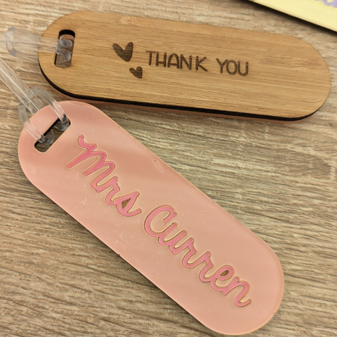 Two keyrings side-by-side, one made of bamboo with a "Thank You" engraving, and the other featuring a personalized peach-colored acrylic tag with the name Mrs. Curren