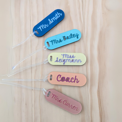 A set of custom teacher keyrings in various colors, including blue, teal, yellow, and peach, with names like Mr. Smith, Mrs. Bailey, and Coach engraved on acrylic tags with a clear bag loop.