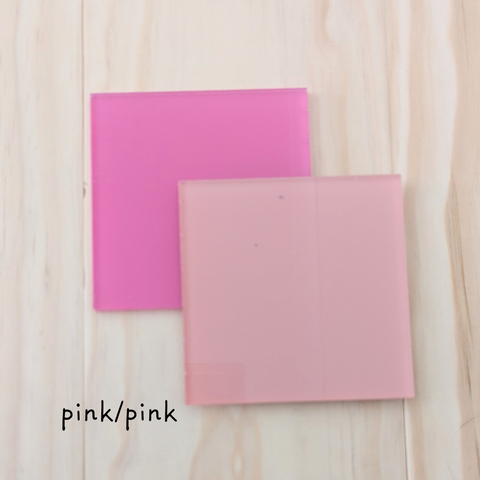 Two square acrylic color samples in bright pink and pale pink, displayed on a wooden background with the label "pink/pink.