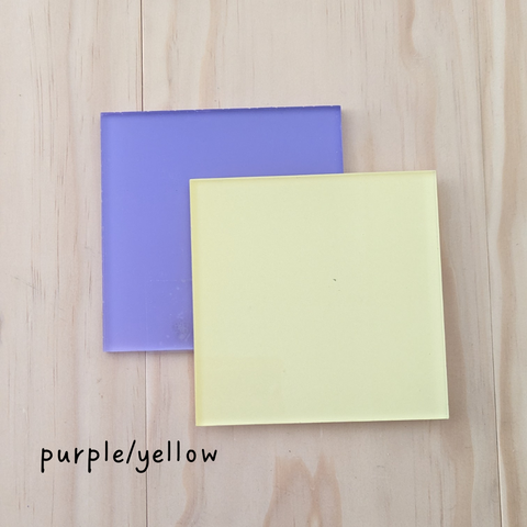 Two square acrylic color samples in purple and yellow, displayed on a wooden background with the label "purple/yellow.