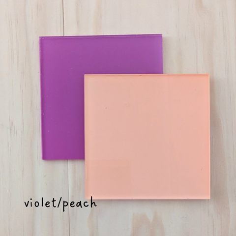 Two square acrylic color samples in violet and peach, displayed on a wooden background with the label "violet/peach.