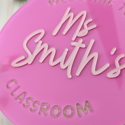 A close-up view of a pink acrylic classroom sign with the text "Ms Smith's Classroom," showcasing the raised lettering and detailed craftsmanship